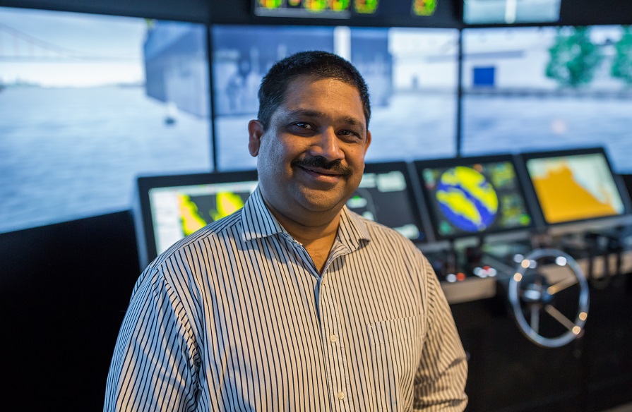 Vivek Saxena, Principal at Strait Area Campus, stands in a marine navigation simulator and smiles.