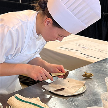Olivia wearing a chefs' hat and coat while practicing her culinary skills.