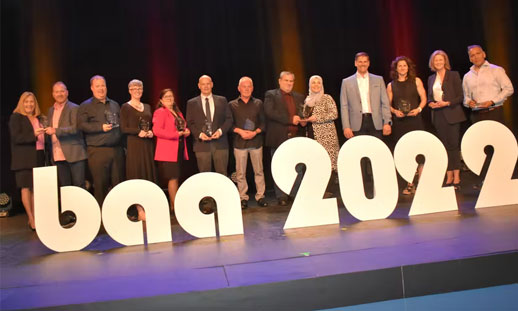 A group of people on a stage with large letters in front of them, which read B A A 2022.