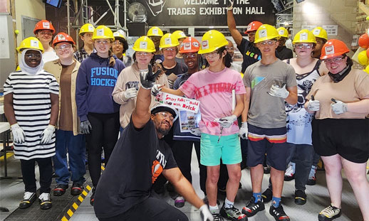 A group of youth wearing yellow and orange construction hats all post for a selfie. 