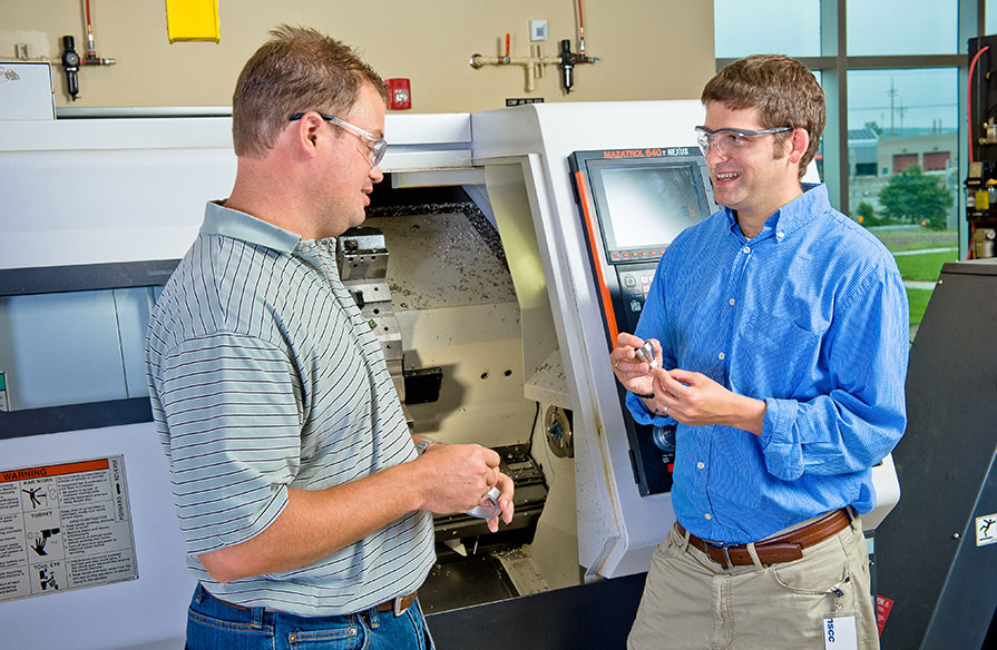 Two NSCC employees looking at a metal machine part.