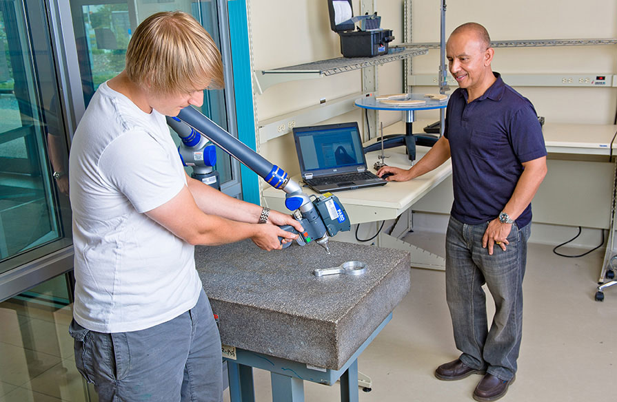 An NSCC employee and student work together on a metal object.