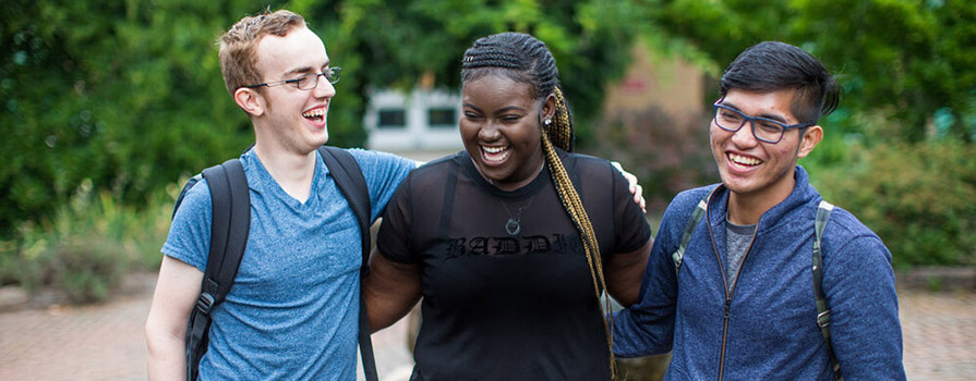 Three students stand with their arms around one another's shoulders while they smile and laugh.