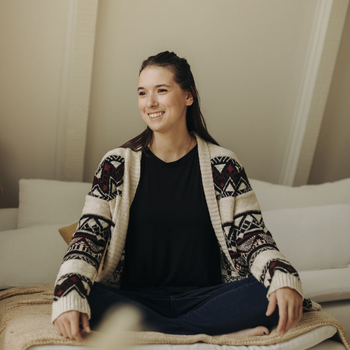 A self-portrait of Hannah Jackson sitting on her bed, smiling into the distance.