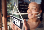 An African Canadian woman smiles as she posts an open sign on the door of her new business.