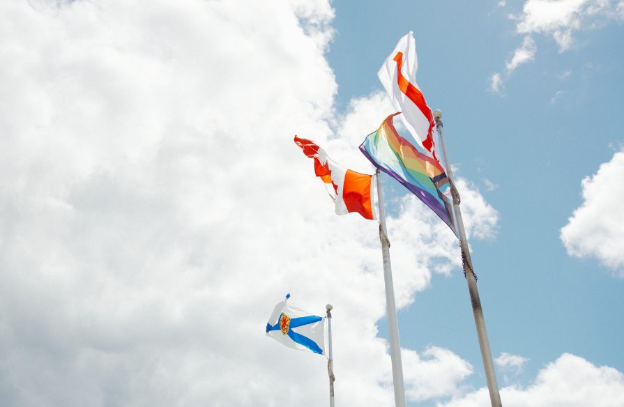 Flags raised and waving in the wind from left to right with the flags of Nova Scotia, Canada, 2SLGBTQ+, and Santéé Mawióómi flag (Mí'kmaq Grand Council Flag)