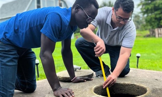 wo men inspecting a well, using equipment to measure water quality or levels.