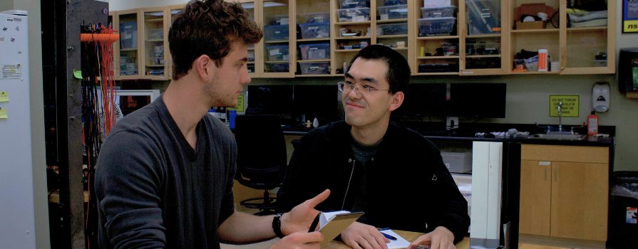 Two students are engaged in a conversation in a lab setting. 