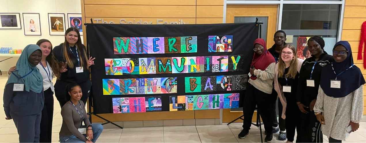 Smiling youth from diverse backgrounds proudly stand around the artwork they created at the exhibit.