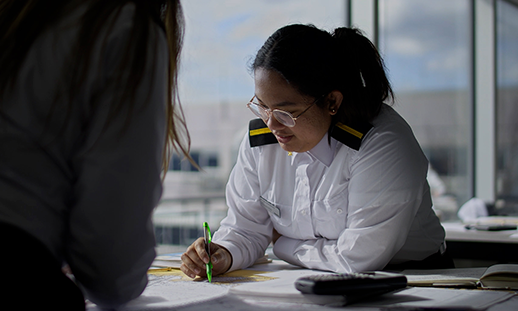 Michaela, Marine Navigation Technology student in a classroom doing chart work at a desk