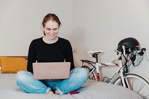 Student sitting on bed while looking at a laptop in Campus Housing at Davis Hall in Truro. 