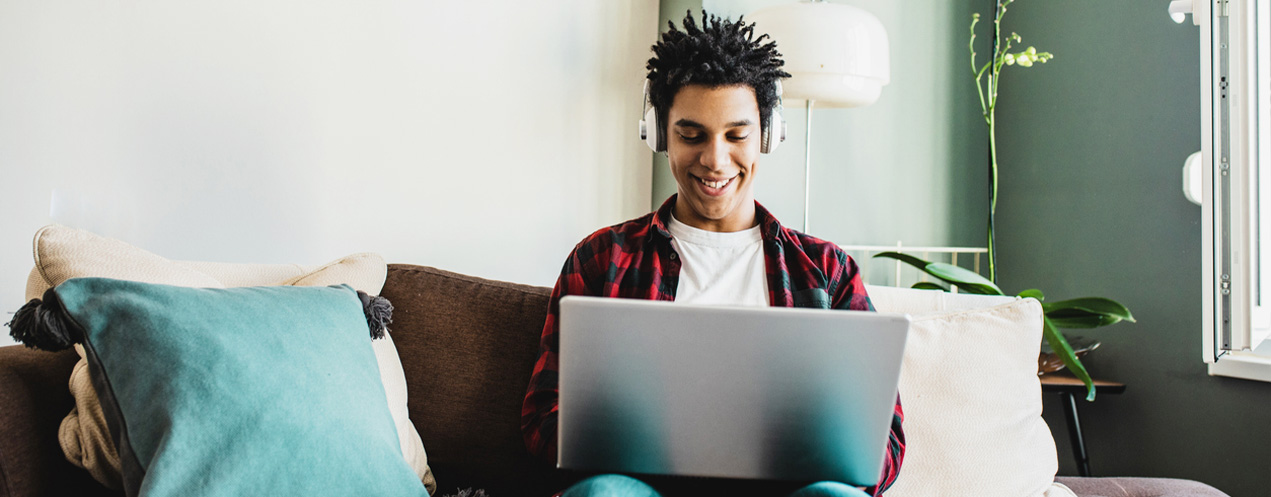 Student wearing headphones sitting on a couch while looking at a laptop.