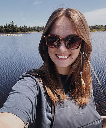 NSCC graduate Mollie smiles at the camera while standing near a lake.