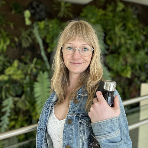 Natasha posing in front of the living wall while holding a waterbottl