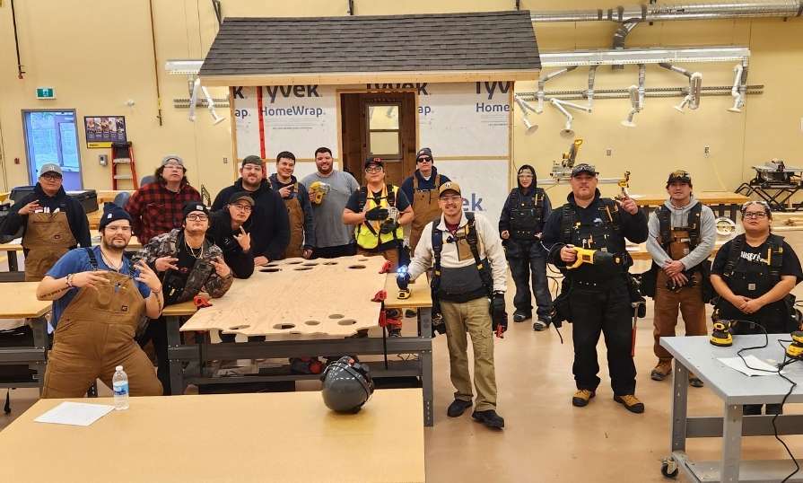 Group of learners posing in a carpentry workshop around desks and a newly built shed.