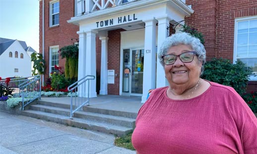 A person is standing outside of town hall, smiling for a photo.