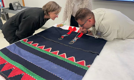 Three people are working on beading on an artifact.