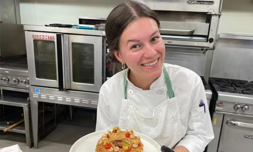 A chef in the kitchen holding a dish they just completed.