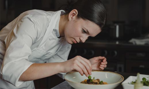 A person is adding finishing touches to a dish they are preparing in the kitchen.