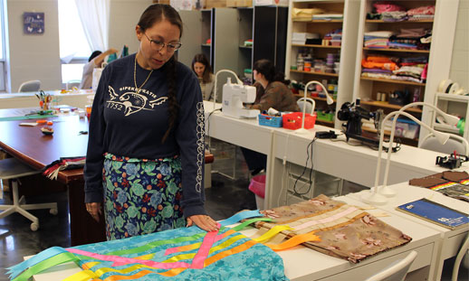 A person is standing in a classroom, working on a ribbon skirt.