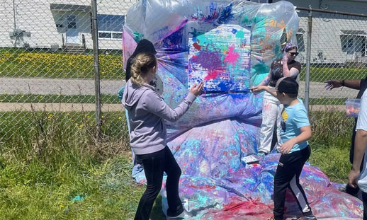 Students throw paint at a mural outside.