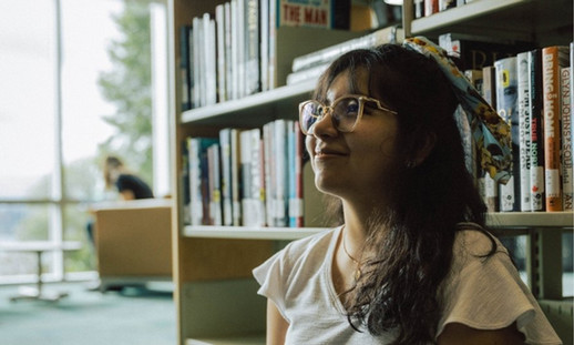 An NSCC student sits in a book aisle of a library space.