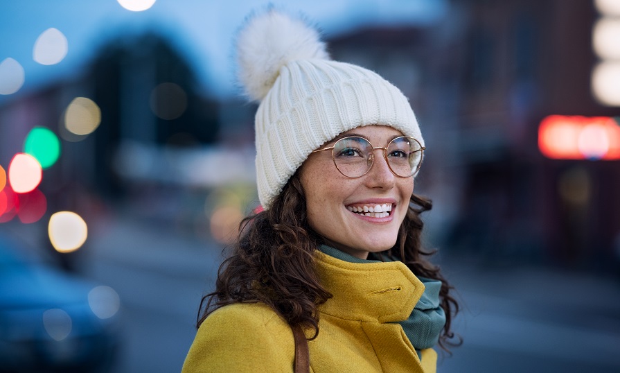 A person is wearing a winter knitted hat, standing outside with a yellow jacket on.