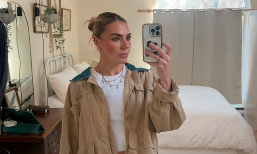 A female is taking a selfie in a mirror with their cellphone in their bedroom.