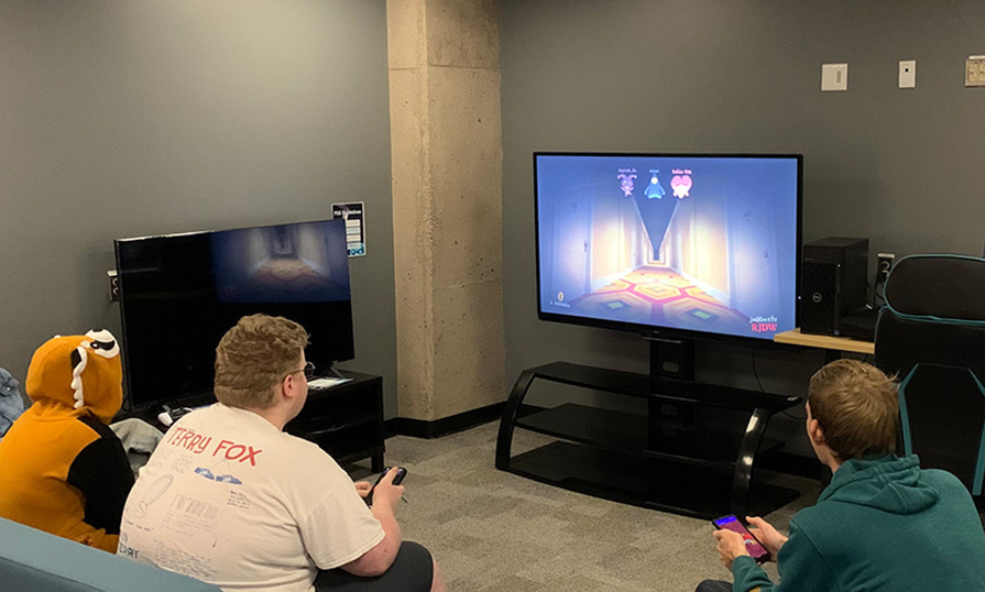 Four people sit on couches in the NSCC Truro Campus Esports Lounge, playing a video game.