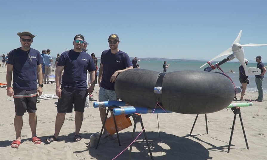 Three people standing on a beach beside a wind turbine.