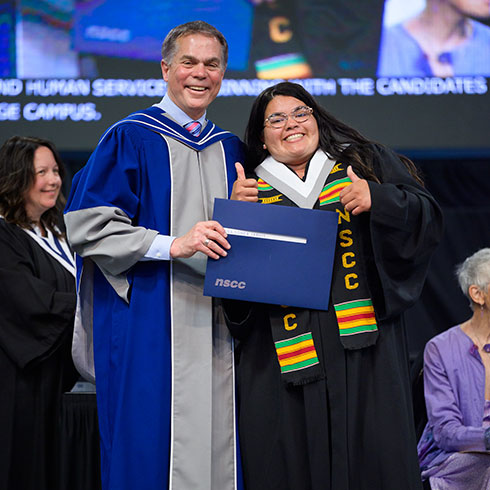 A student stands on a stage with the President of NSCC during a convocation ceremony.