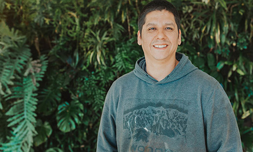 An individual wearing a grey hoodie is smiling towards the camera.