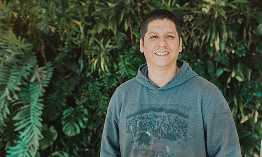 A student wearing wearing a green hoodie sweatshirt smiles toward the camera. 