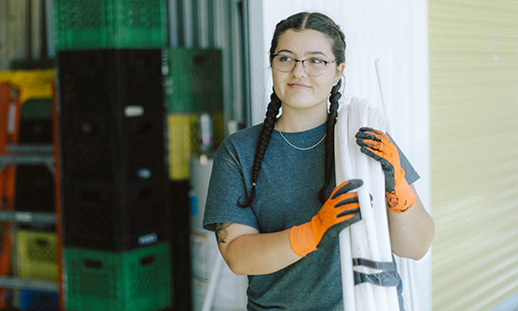 An NSCC Plumbing student carries a role of hose over her left shoulder while smiling.