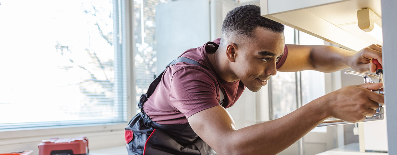 A student holds a screwdriver and works on a plumbing project.