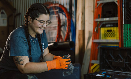 A student wearing glasses and safety gloves holds a tool in a workshop.