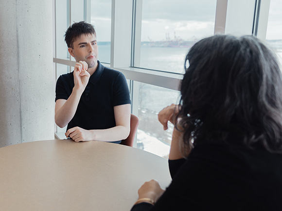 A student shares a sign in American Sign Language (ASL) with another student while seated at a table at an NSCC campus.