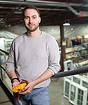 Cole stands on an elevated walkway in an large industrial building.