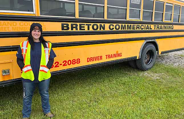 A woman in a reflective vest smiles in front of a school bus.