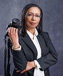 A headshot of Sabrina who folds a camera jauntily over her shoulder.