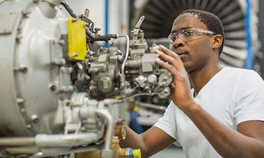 An aircraft maintenance diploma student wearing safety goggles works on a plane’s engine.