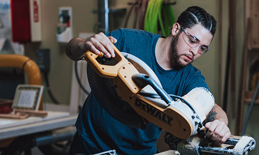 A Nova Scotia carpentry programs student using a machine to cut a piece of wood.