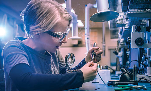 A woman sits at a desk and works on electronic engineering equipment in a campus learning lab.