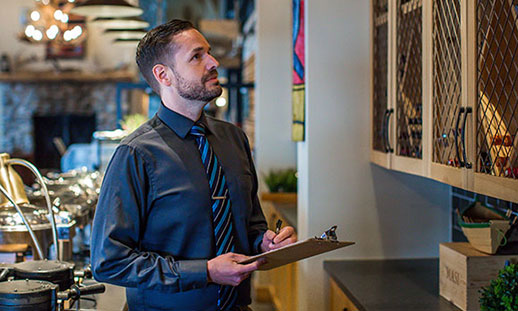 A hospitality and tourism student holding a clipboard checks inventory in a restaurant.