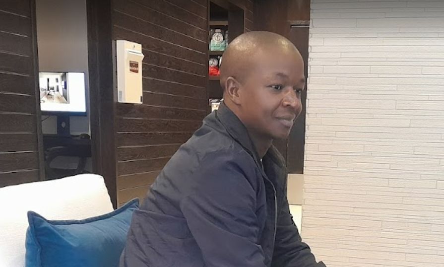 Geofrey sitting indoors, smiling, during an educational study tour.