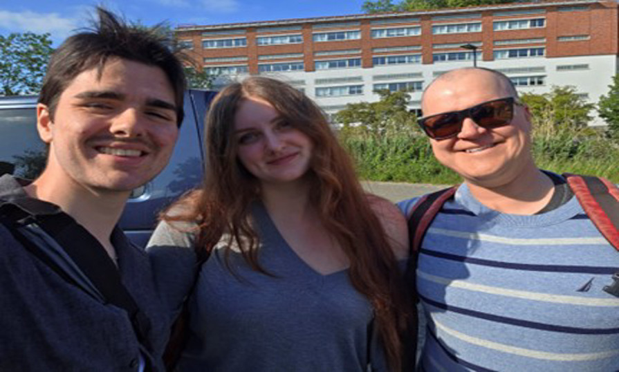 Michael and two students smiling outdoors on a sunny day