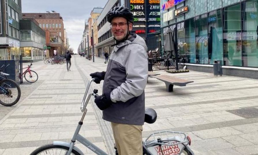 Wayne McKay smiles while holding a bike on a pedestrian street in Finland.