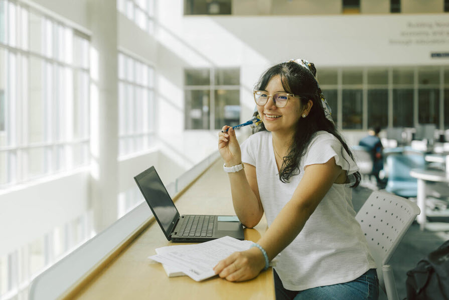 person sitting at window working with books and laptop